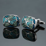 Pair of silver cufflinks with green and blue pattern on a reflective surface