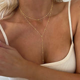Woman wearing a gold lariat necklace with a beige top.