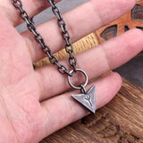 Hand holding a necklace with a triangular pendant on a wooden surface