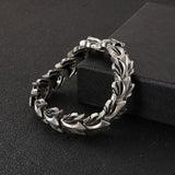 A silver-toned metal bracelet with a textured leaf pattern, displayed on a black textured surface next to a black box.