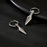 A pair of silver-toned hoop earrings with arrow-shaped charms, displayed on a textured black surface with a curved black prop.