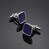 Pair of silver cufflinks with blue stones on a reflective black surface.