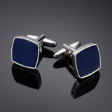 Pair of blue square cufflinks with silver borders on a reflective black surface.