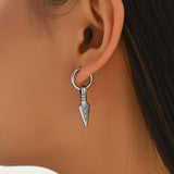 A close-up of a person's ear wearing a silver hoop earring with a dangling arrow-shaped charm.