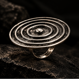 A silver-toned ring with concentric circular ridges and a raised central dome, photographed close up on a dark textured surface.