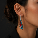 A close-up of a woman's ear wearing a long, teardrop-shaped dangle earring with a silver-toned metal top and a colorful inlay featuring turquoise blue, red, and black marbled patterns.