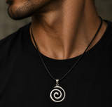 A close-up of a man's neck and chest wearing a silver spiral pendant necklace on a black cord over a black t-shirt.