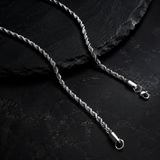 A silver-toned twisted rope chain necklace with a lobster clasp, displayed on a dark textured slate surface.