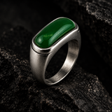 A silver-toned ring with a large, polished green rectangular stone, displayed on a dark textured rock surface.