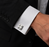 A close-up of a man's wrist wearing a black suit jacket with a white French cuff, featuring a silver-toned four-button cufflink.